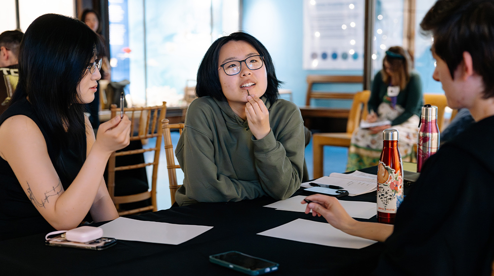 Three people sit at a table chatting.