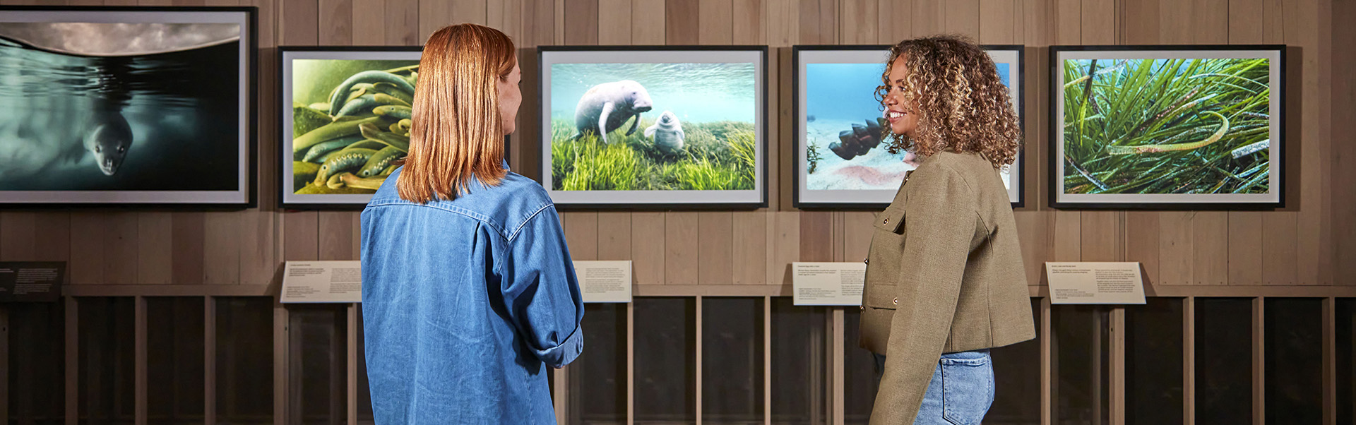 Two women stand in front of pictures of the Wildlife Photographer of the Year exhibition