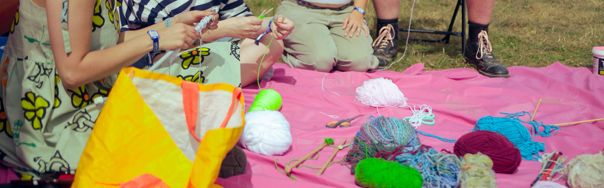 Four people sit around a pink blanket with wool and crochet needles during a workshop