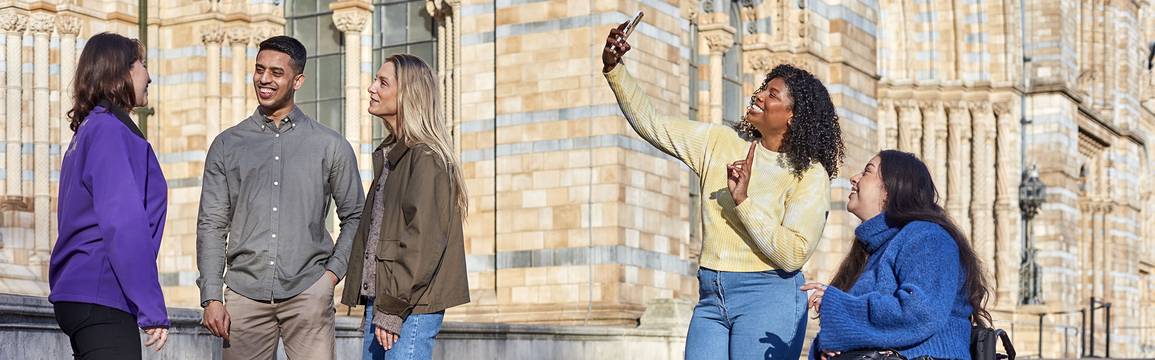 Three people talk as two others take a selfie outside Waterhouse Building