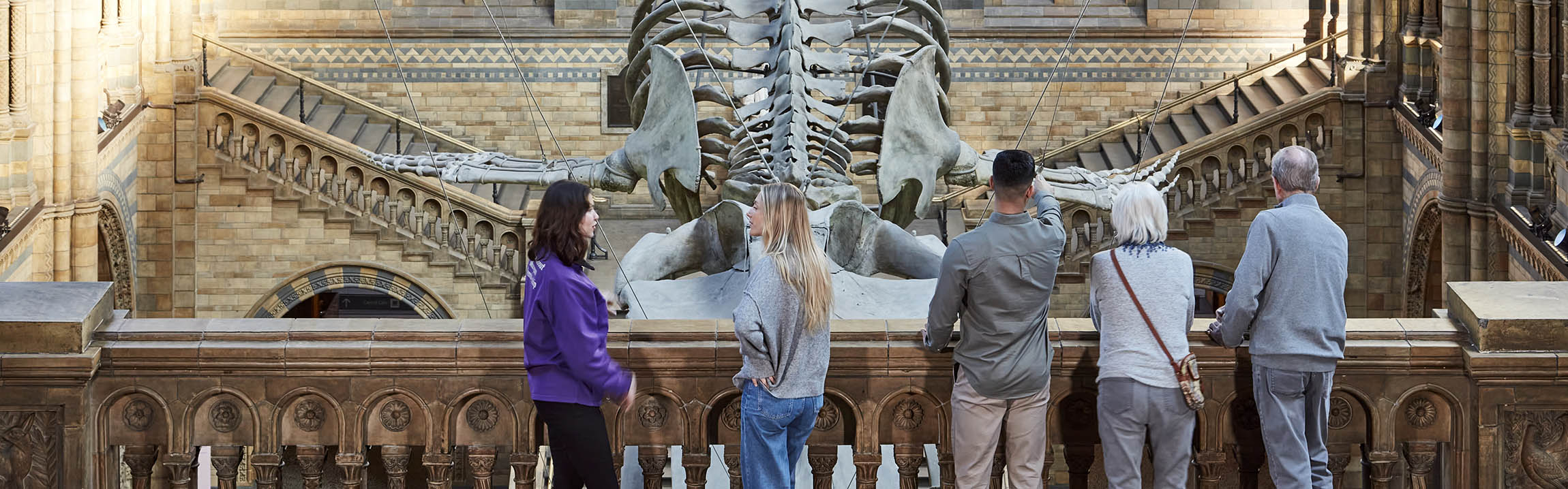 Five people stand on a balcony at Hintze Hall overlooking Hope the blue whale