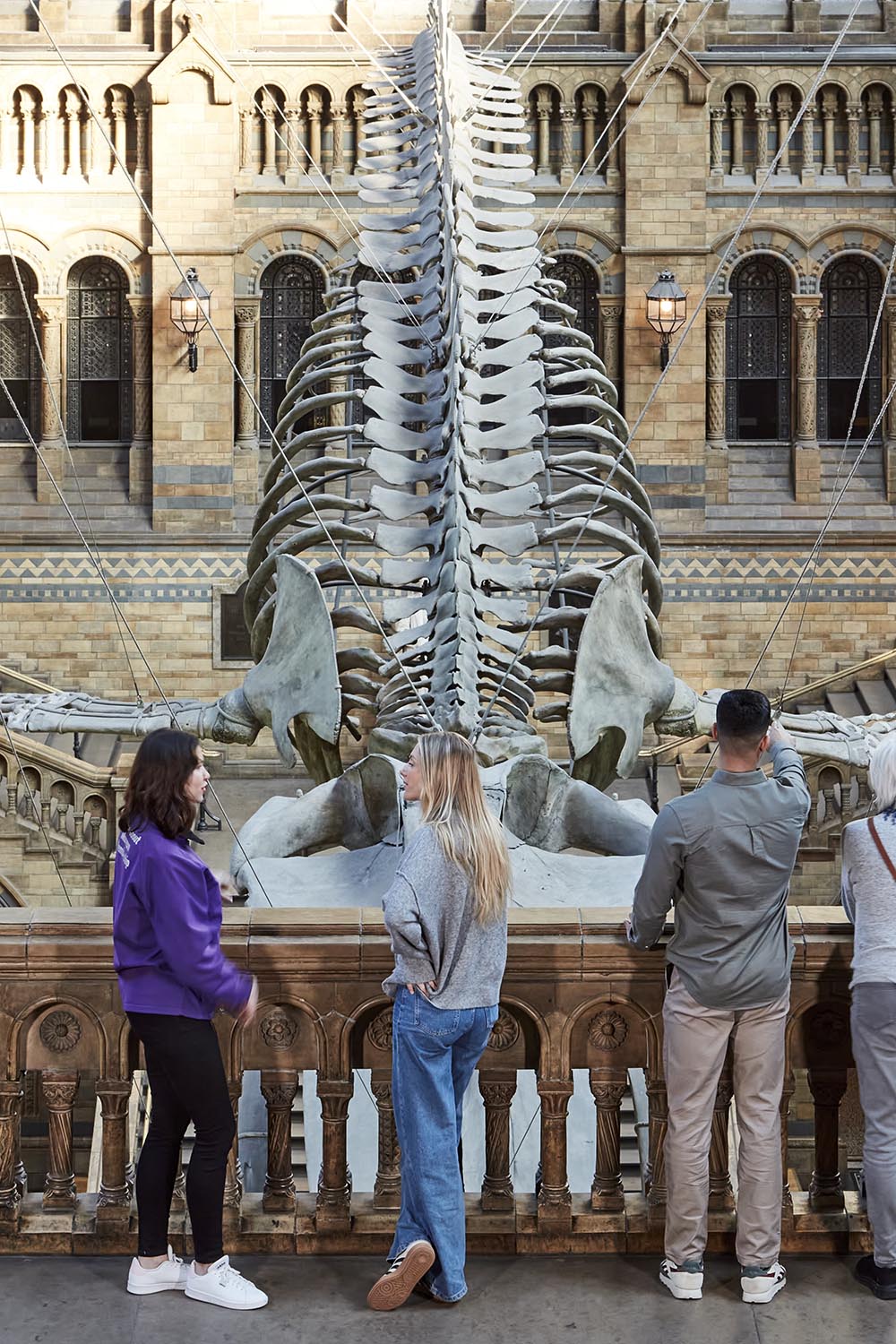 A tour guide talks to a group of people on a balcony at Hintze Hall overlooking Hope the blue whale