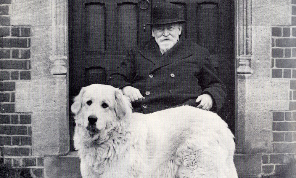 A black and white photo of Walter Rothschild wearing a hat and sitting behind a big labrador