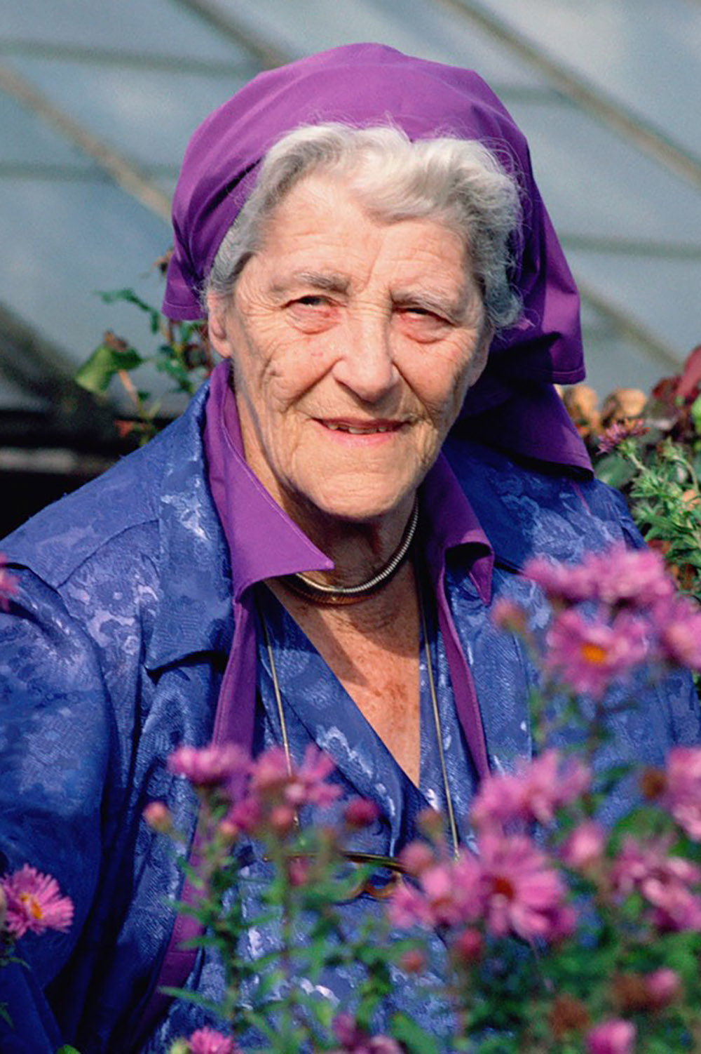 Miriam Rothschild wearing a purple headscarf and surrounded by pink flowers