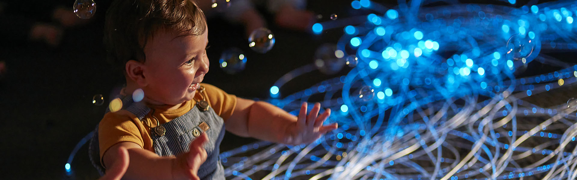 A baby sits sits in front of blue lighting as an extended hand helps him  