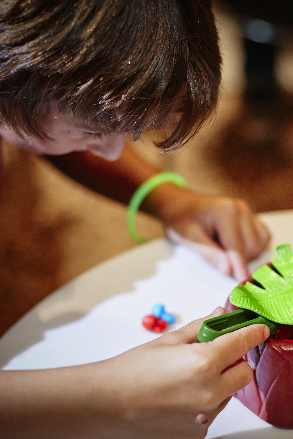 A boy leans over a small green toy dinosaur