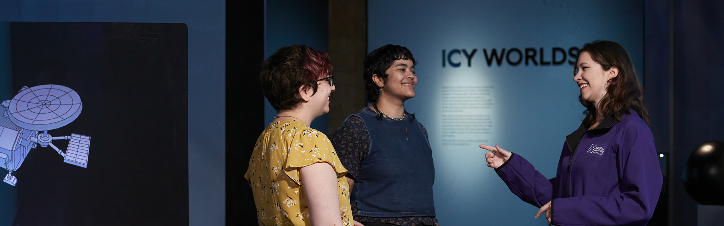 A tour guide talks to two people at the Space exhibition in front of a sign that reads Icy Worlds