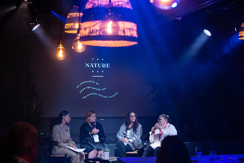 Four women sit under lights on a stage at the nature bar cop26