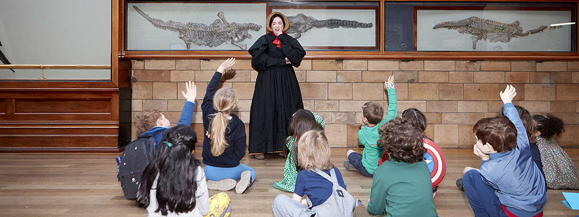 A woman dressed as mary Anning talks to a  group of children in front of fossils