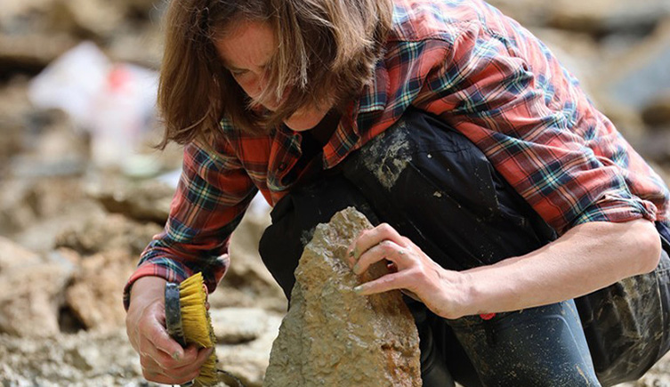 A woman scrubs a rock in a muddy puddle 