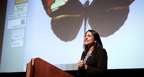 A scientist speaks from a podium in front of a projected image of a butterfly