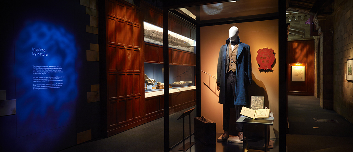 A photo taken inside the Fantastic Beasts: Wonder of Nature exhibition space. A manequin dressed in a blue coat is inside a glass cabinet surrounded by curiosities from the natural world. 