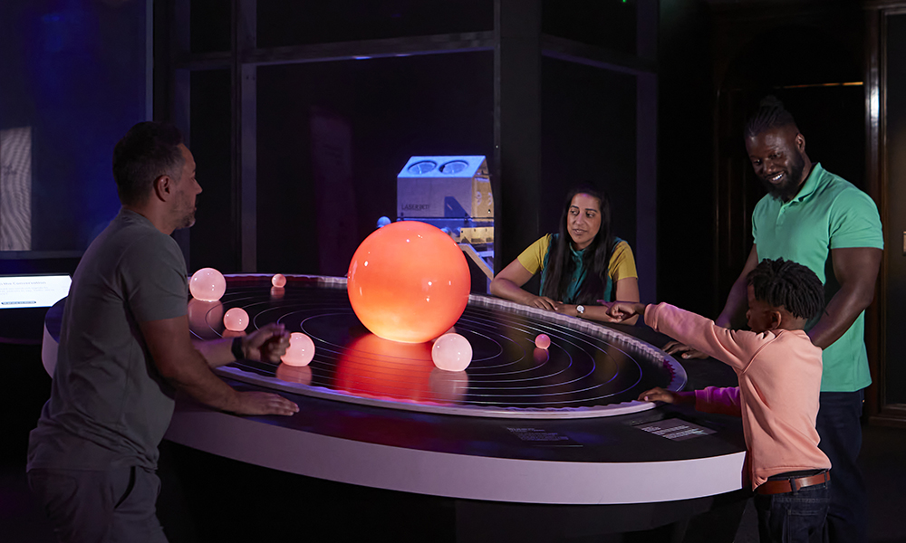 Four people stand around a model of a solar system