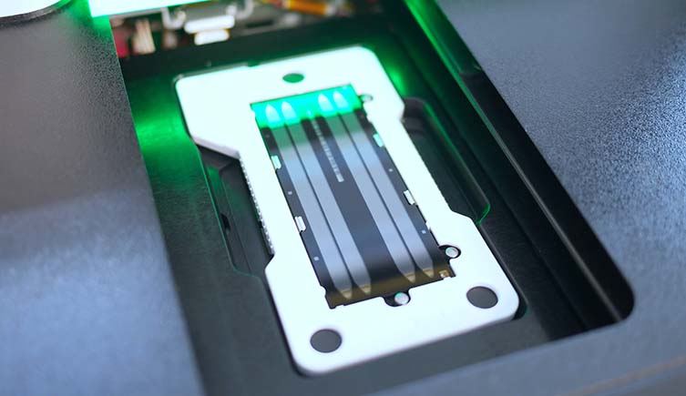A green light shines on a rectangular flow cell from a next generation DNA sequencer.