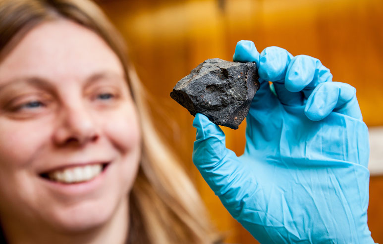 Professor Sara Russell holding a meteorite in a gloved hand