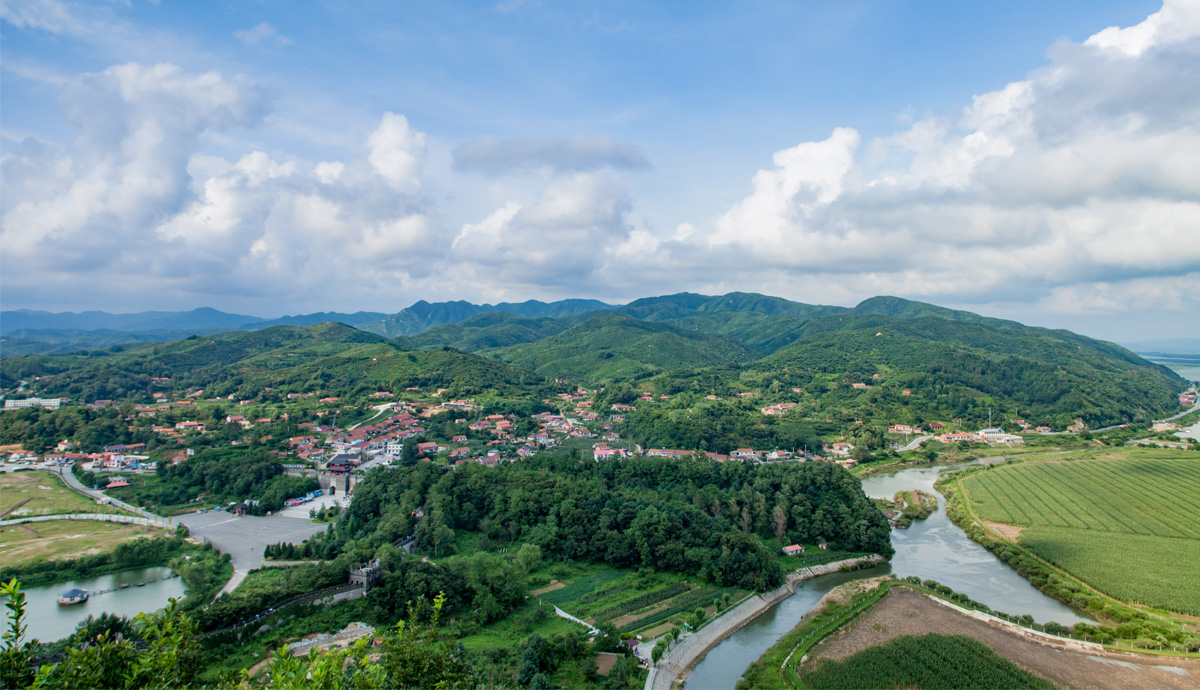 An aerial view of a location in the Liaoning Province. There are mountains, trees and a river