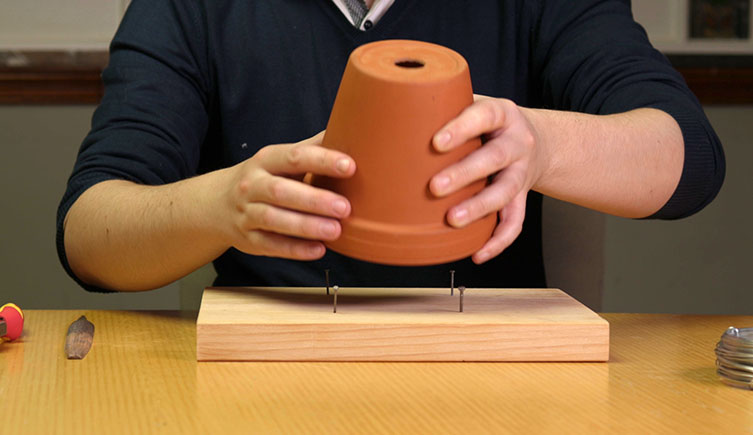 Placing the pot on the piece of wood, between four nails