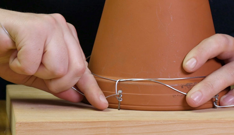 Close up showing wire secured around a pot and being wound around a nail
