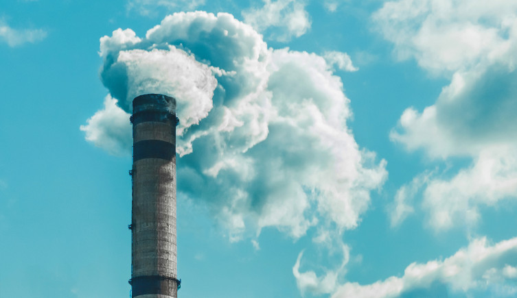 An industrial chimney releasing gas into a blue sky