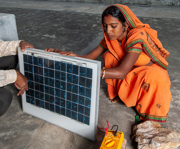 A woman in an orange sari sets up a small solar panel