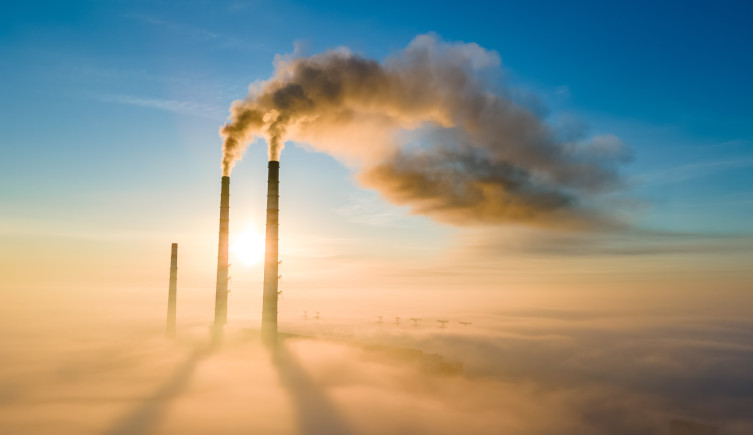 Vapour is emitted from two tall chimneys above a sea of cloud, with the sun behind them.