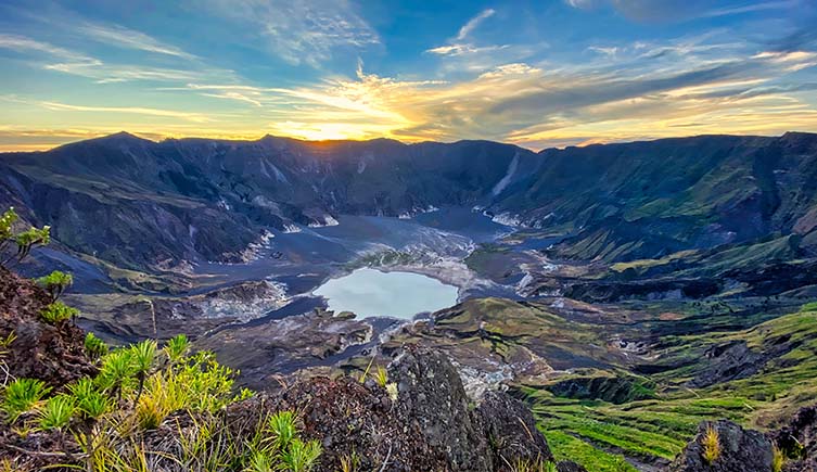 A large circular caldera with rocky sides reaching down towards a lake in the centre.