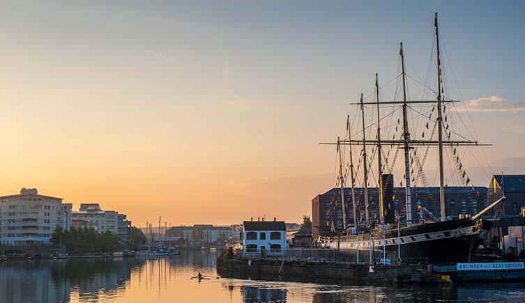 Sunset over Bristol harbour, with the masts of the SS Great Britain rising into the sky.