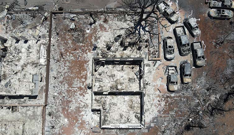 A burnt out house and cars seen from above, stained grey with ash.