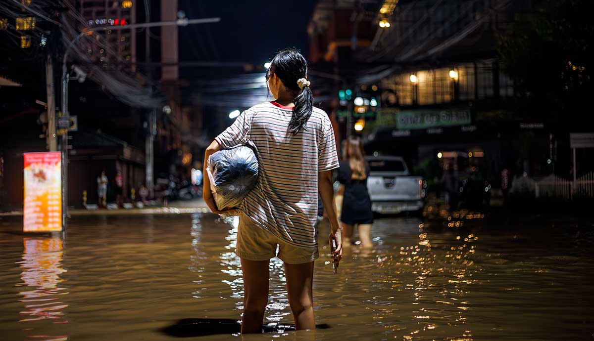 A woman standing knee deep in brown flood water in the middle of an urban street at night. 