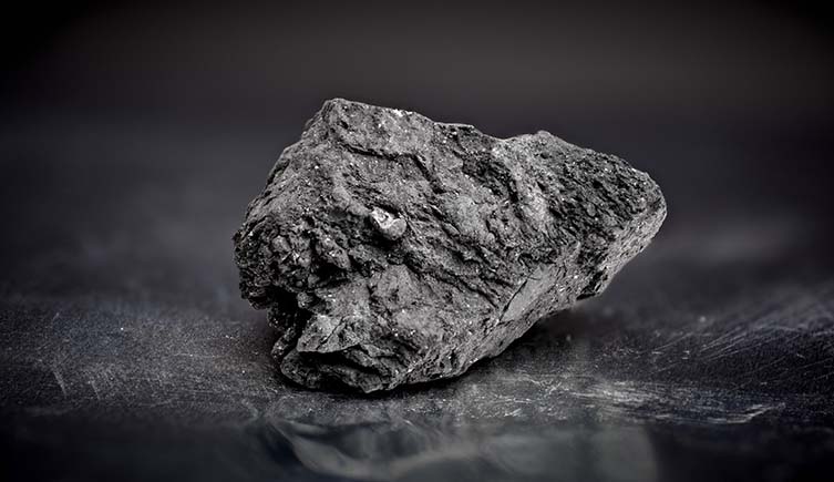 A photo of a black lump of the Winchcombe meteorite on a reflective surface.