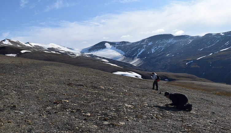 A landscape photograph showing two people hunting for fossils in the foreground with mountain ranges of Spitsbergen in the background 