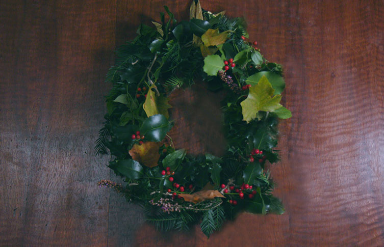 A finished wreath is hung on a wooden wall with a ribbon
