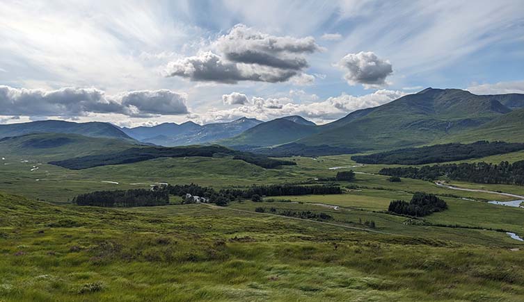 Clouds drift among blue skies over the green hills of the Scottish Highlands.
