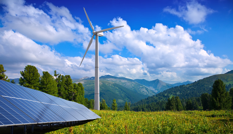 A green field with solar panels and a wind turbine in the background.