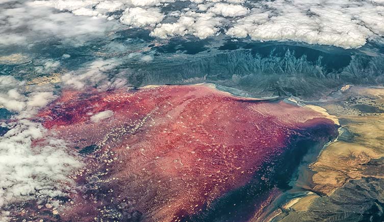 An aerial photograph of a red lake, with clouds floating above it.