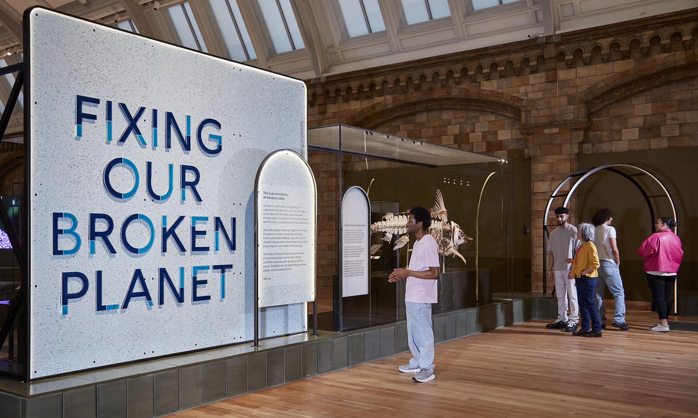 A big sign at the entrance of the exhibition space reads "Fixing Our Broken Planet" in capital letters, as people stand nearby.