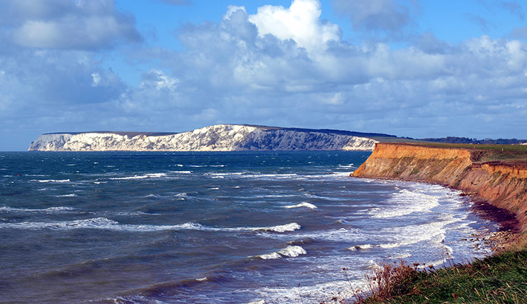 A view across the southern coast of the Isle of Wight, showing reddy/brown cliffs in the forground changing to white cliffs in the background. 