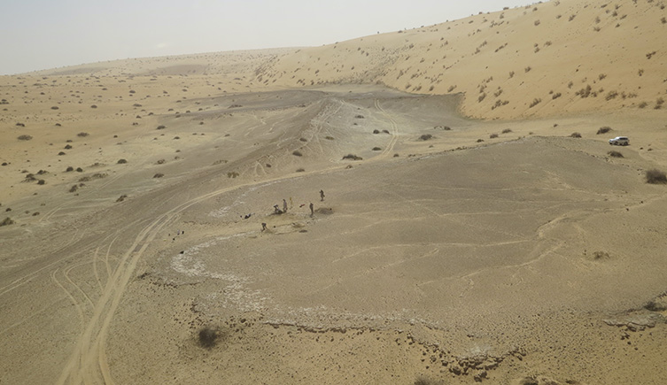 A view looking down on the desert between two sandunes, showing the outline of an ancient lake in a darker coloured sediment. 