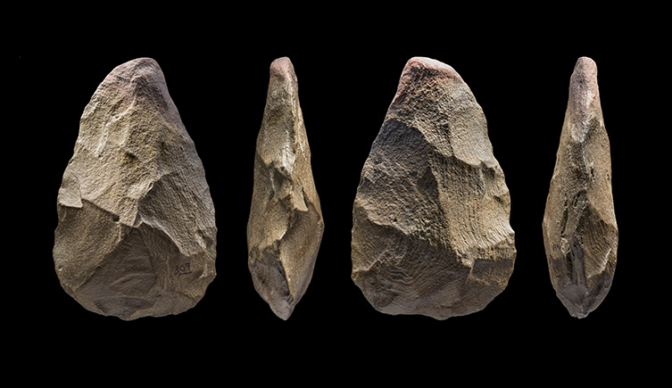 A handaxe, showing clear signs of being worked into a point is shown on a black background. 