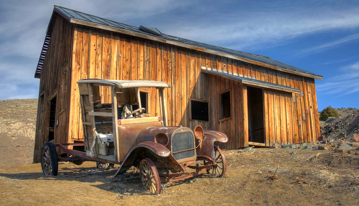 A photo of a rusting old-fashioned car next to an abandoned wooden building in Berlin-Ichthyosaur State Park, USA.