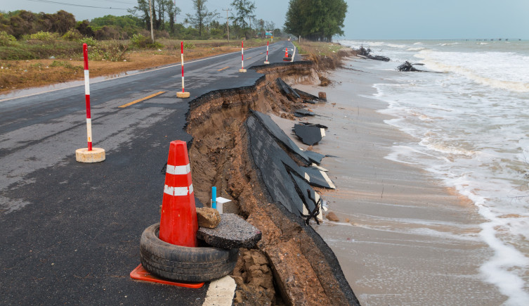 A partially collapsed road is coned off as water washes on the nearby beach