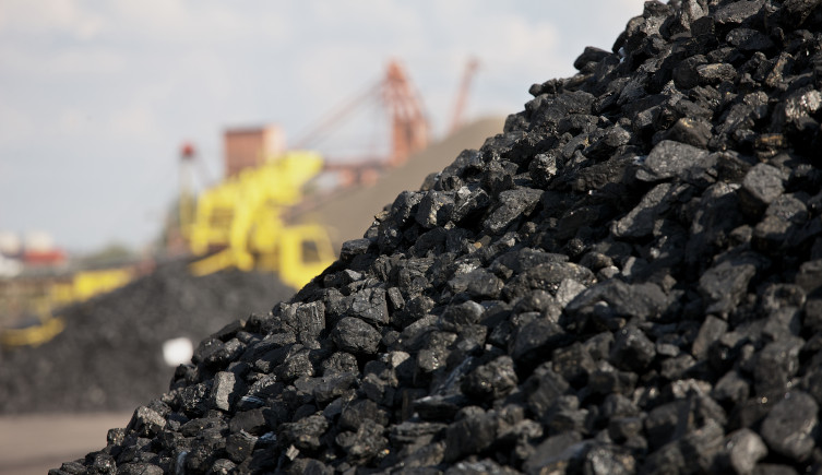 A pile of coal in front of mining equipment in the distance