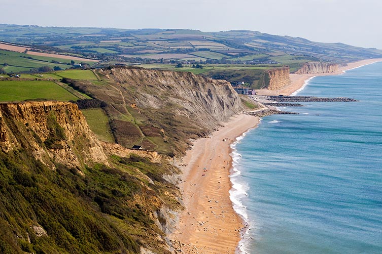 Aerial view of Jurassic-age UK coastline, showing fields on top of cliffs that descend to sandy beaches