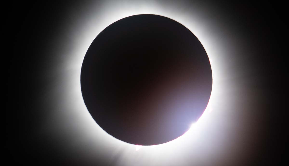 The black disc of the Moon sits in front of the Sun during a solar eclipse, with a corona of light peeking out from around the sides.