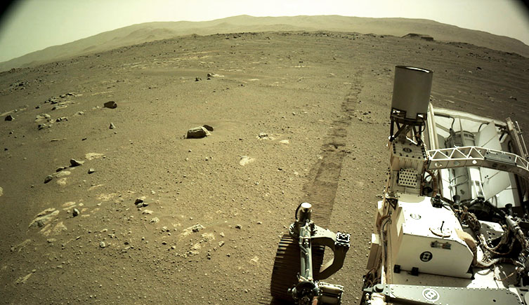 A photograph taken by the Mars rover, showing the landscape of the planet with some of the rover caught in the bottom right corner. 