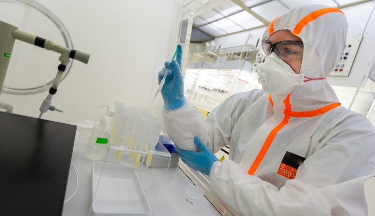 A scientist in protective clothing holds a pipette in a fume cupboard