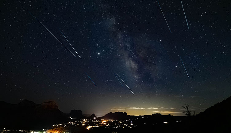 Streaks of light cross the night sky above a lit up city.  
