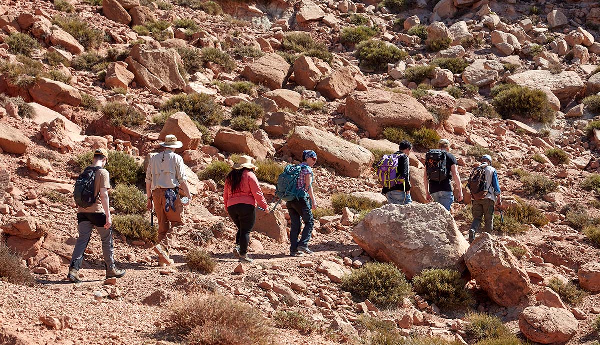 A group of scientists hikes up the side of a boulder-strewn mountain.