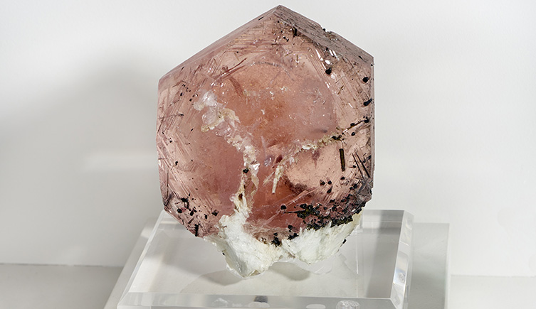 A light pink hued crystal with flecks of black and grey impurities within.