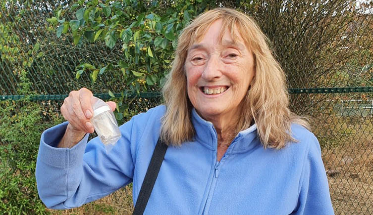A picture of Barbara Mulligan smiling at the camera whilst she holds up a small vial containing the new moth named after her. 